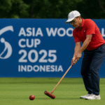 Pemain woodball memukul bola dengan mallet di lapangan hijau, dengan spanduk Piala Asia Woodball 2025 Indonesia di latar belakang.