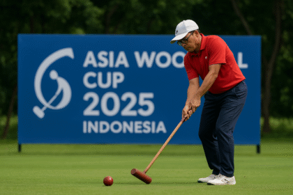 Pemain woodball memukul bola dengan mallet di lapangan hijau, dengan spanduk Piala Asia Woodball 2025 Indonesia di latar belakang.