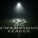 Logo Liga Champions UEFA di tengah lapangan yang gelap, melambangkan drama dan ketegangan.
